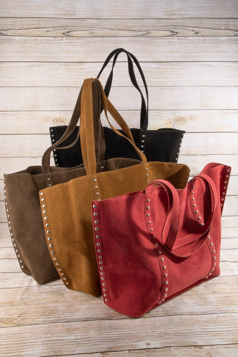 Three suede handbags in brown, red, and black on a wooden surface